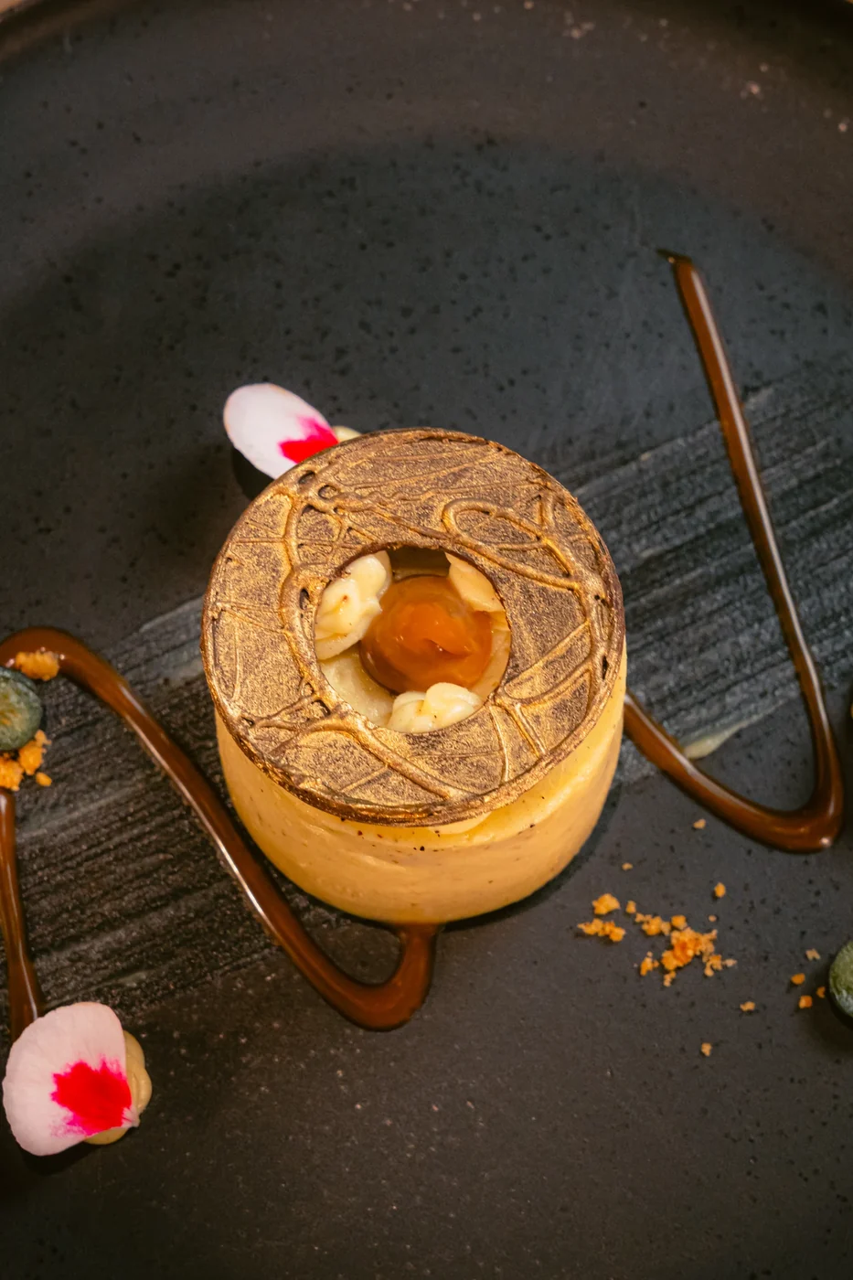Postre con detalle dorado y pétalos sobre un plato oscuro